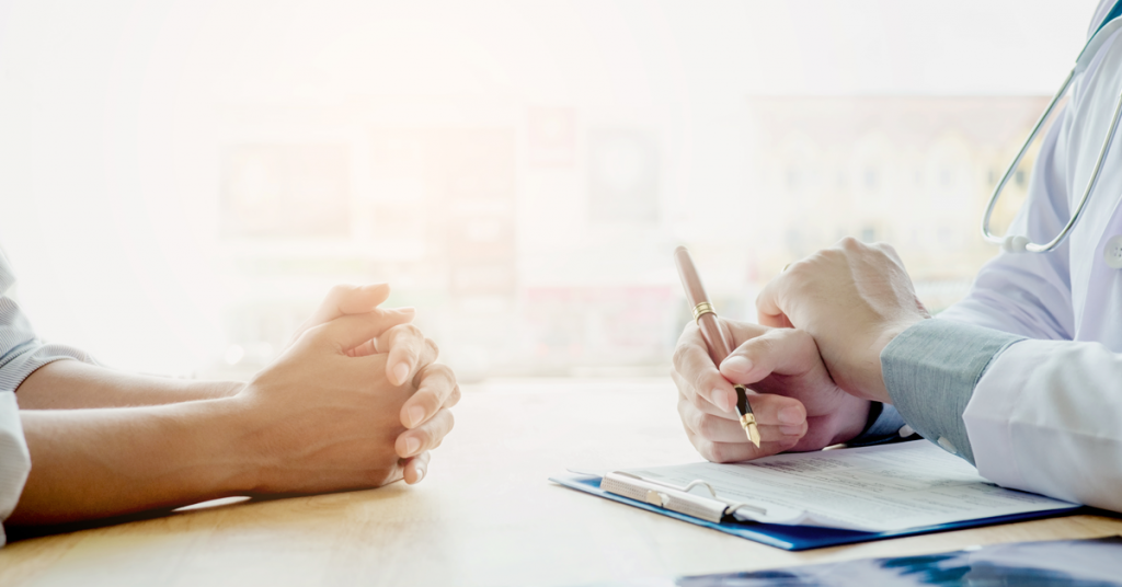 Side close-up view of two people's hands resting on a table across from one another.