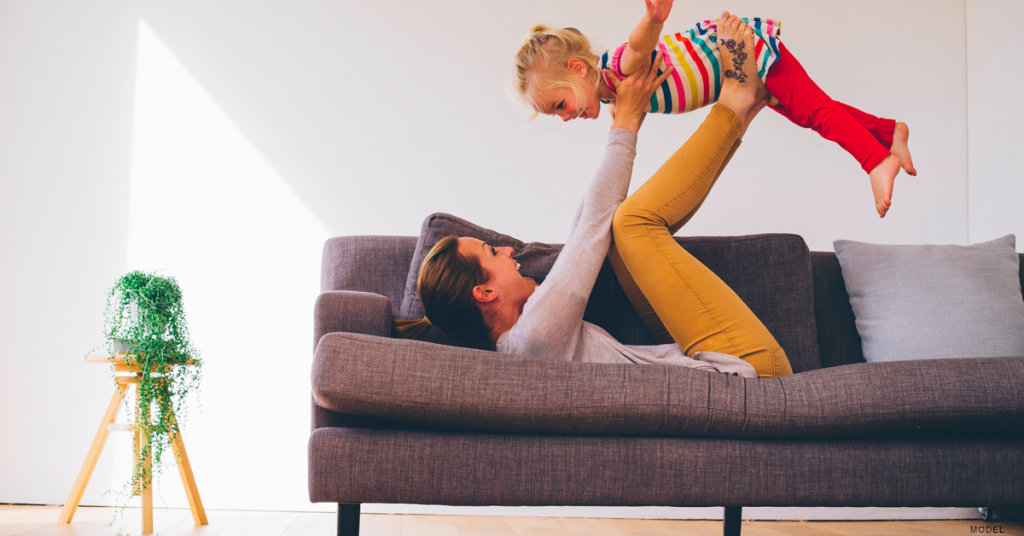 Woman lying on her back on a sofa with her legs up, lifting a child in the air.