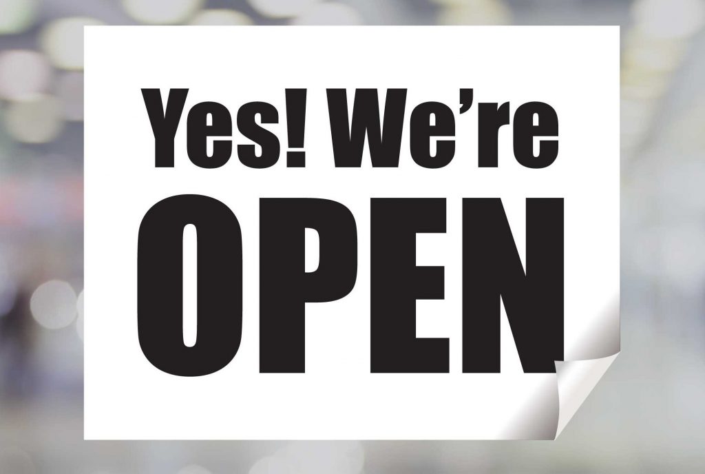 White sign with black lettering that says Yes! We're Open.