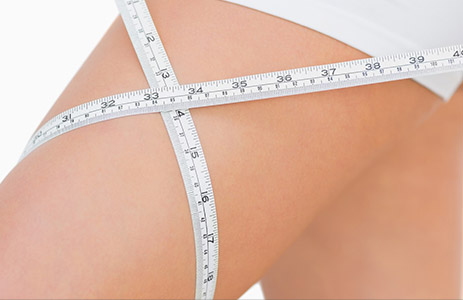 Close-up of a white measuring tape wrapped around an upper thigh.