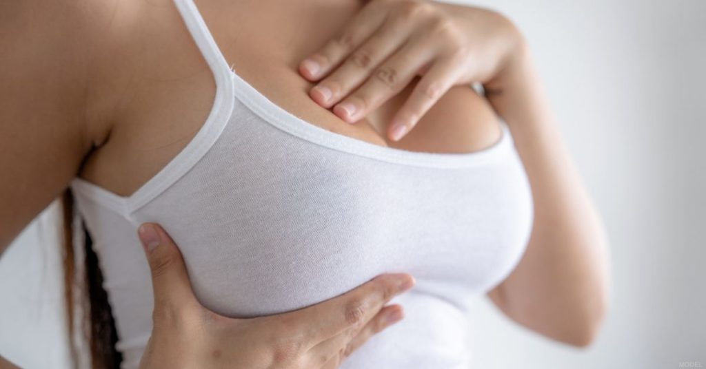 Woman in a white tank top with her hand on her chest (model)